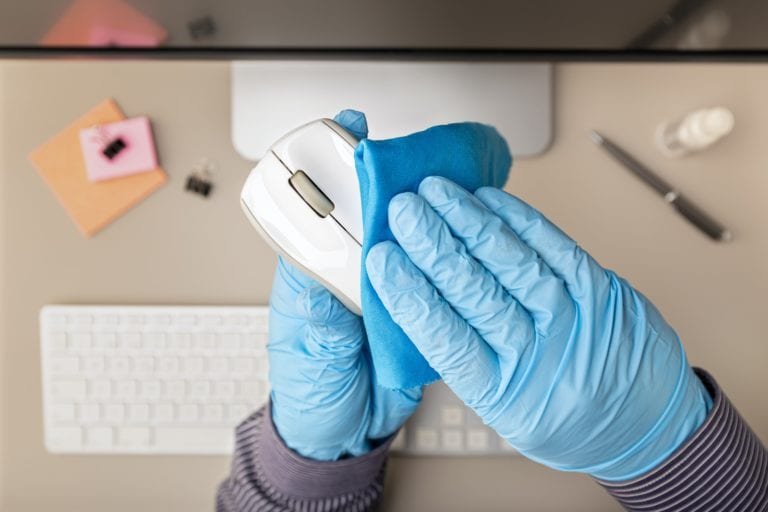 Hand with protective glove cleaning a computer mouse with disinfectant
