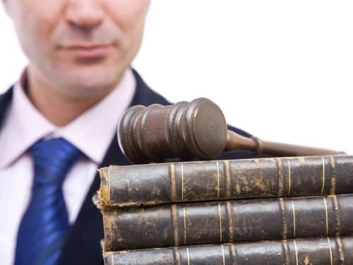 Homem ao fundo, vestindo terno e gravata, tendo à frente martelo de madeira de juiz sobre livros de legislação de terceirização de serviços